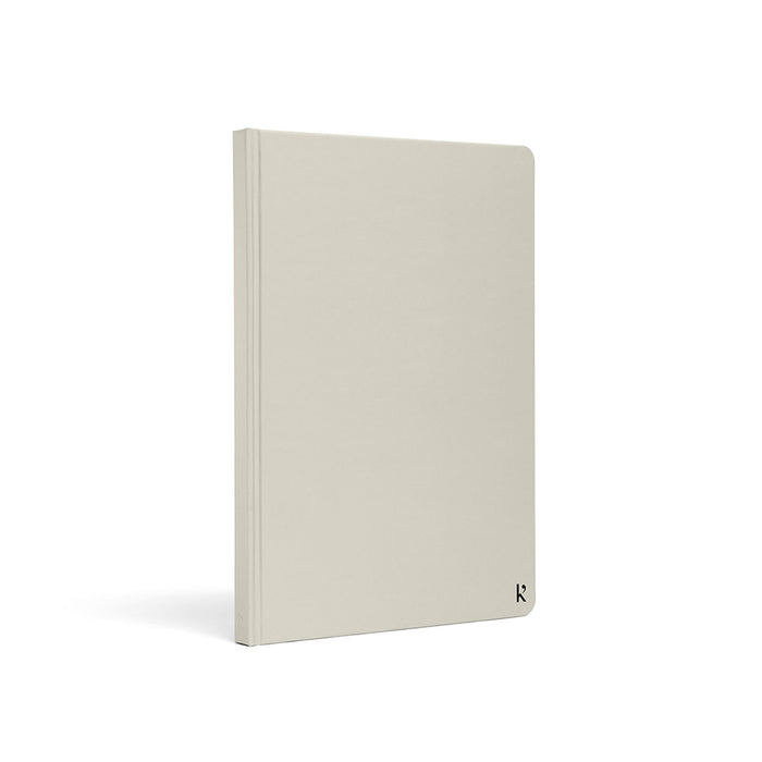 Karst A5 hardcover stone paper notebook in light beige with rounded corners and subtle logo detail, standing upright on a light gray background.