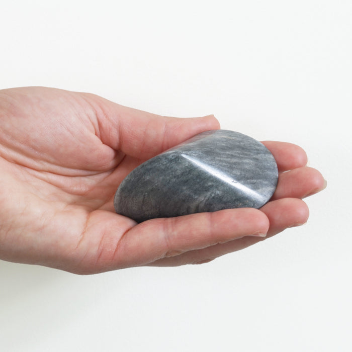 Hand holding a smooth light gray marble oloid sculpture, shown against a clean white background to highlight its size, shape, and natural stone texture.